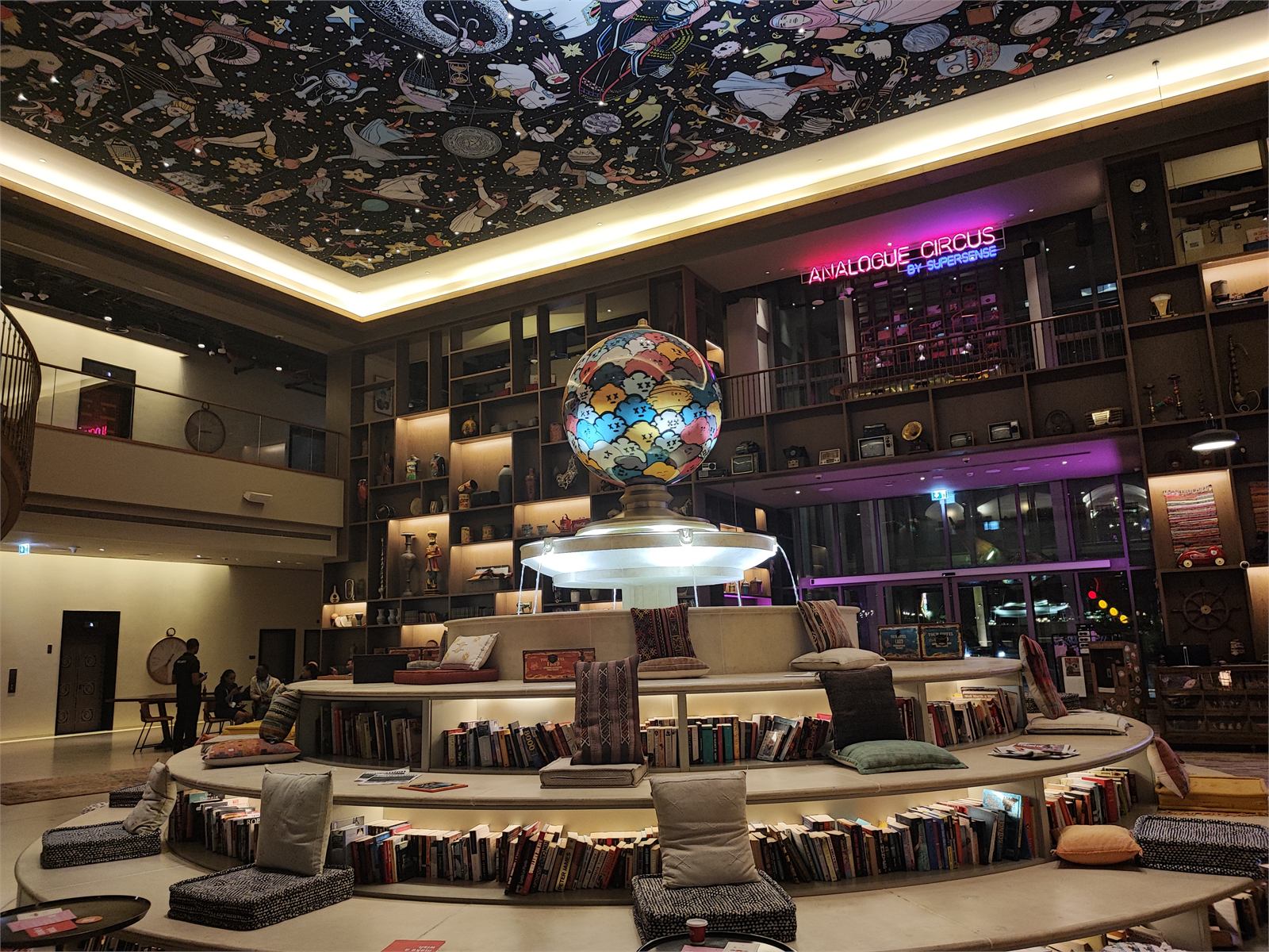 Analogue Circus interior with a colorful ceiling and book-lined seating